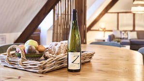 Una botella de vino, un bol de fruta y una hogaza de pan sobre una mesa en una habitación con vigas de madera y una lámpara colgante.