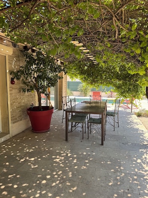 Eine Terrassengruppe mit Tisch und Stühlen, umgeben von einem großen Kübelbaum und einer Steinmauer.