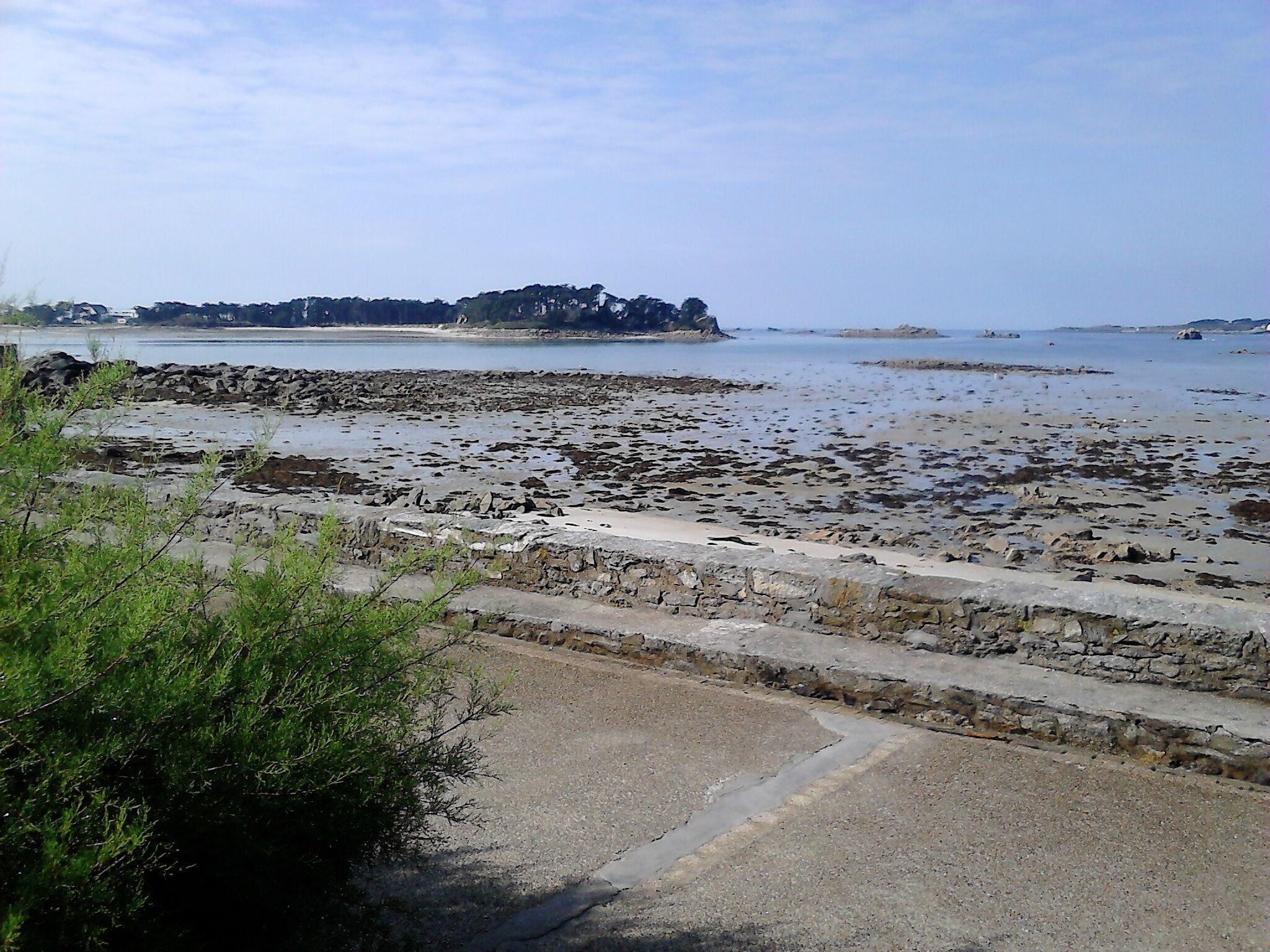 Eine Küstenstraße mit steinigem Strand und einer Steinmauer.
