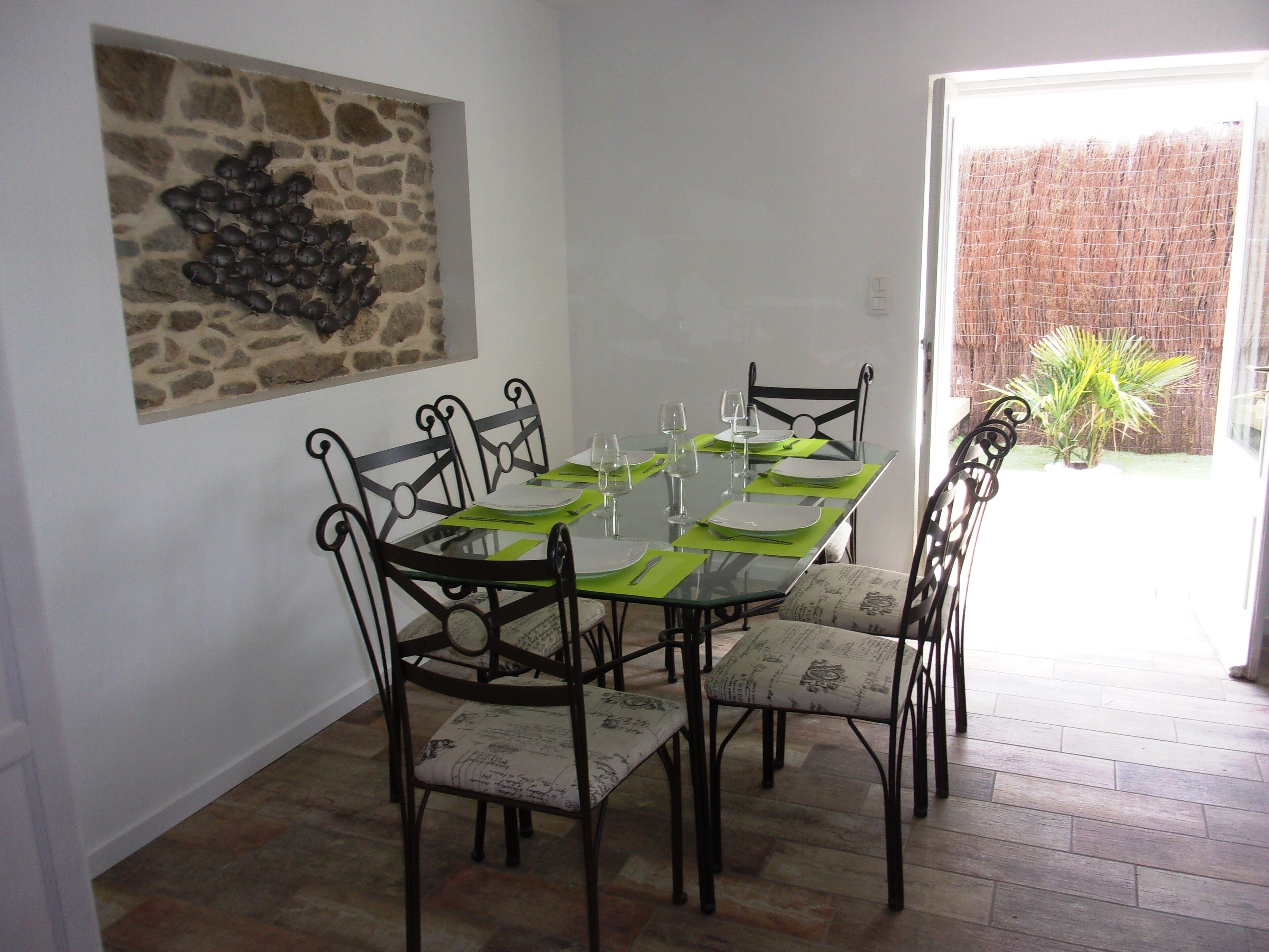 Un coin repas avec une table en verre dressée pour six personnes, entourée de chaises en métal noir ornées de coussins à motifs.
