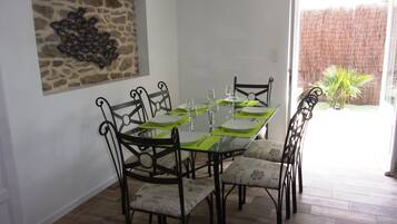 Un coin repas avec une table en verre dressée pour six personnes, entourée de chaises en métal noir ornées de coussins à motifs.