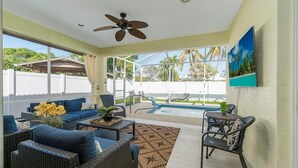 A sunlit patio with wicker furniture, a ceiling fan, and a view of a swimming pool. - March openings! Heated pool, 3 + den bdrm luxury, beach vacation gem! (Naples)