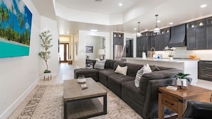 A spacious living area with a dark-colored sectional sofa, a coffee table, and a dining table. The kitchen features dark cabinets and stainless steel appliances. - March openings! Heated pool, 3 + den bdrm luxury, beach vacation gem! (Naples)