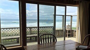 A room with a large window overlooking the ocean, a wooden table, and two chairs. - Classic Honeymoon Beach Cottage. Private, Romantic, Oceanfront.  Pet friendly. (Waldport)