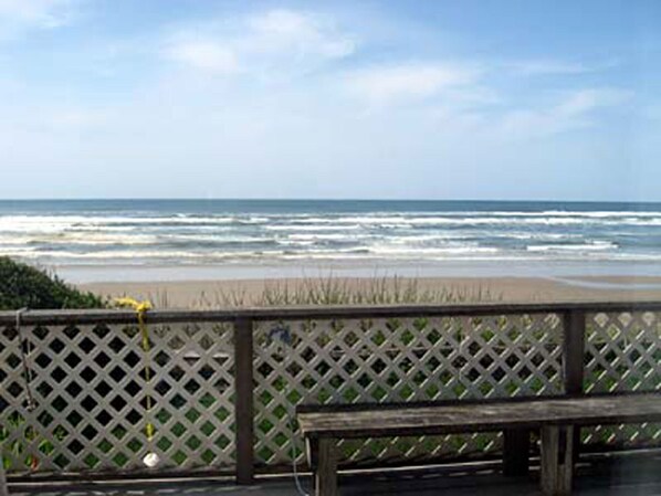 A wooden deck with a bench overlooking a beach with waves.