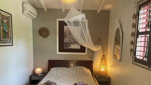 Een net opgemaakt bed met hemelbed, een wandairco, een ingelijst kunstwerk en een bedlampje.