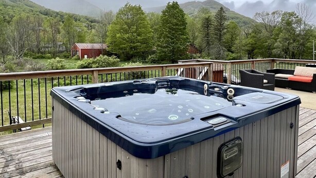 Un jacuzzi en una terraza de madera con vistas a una montaña y árboles.