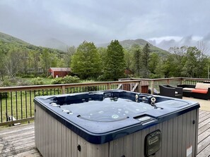 Un jacuzzi en una terraza de madera con vistas a una montaña y árboles.