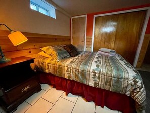 Un dormitorio con cama, mesita de noche, lámpara, ventana y armario.