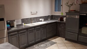 A modern kitchen with dark cabinets, a stainless steel refrigerator, a built-in oven, and a window with a view.