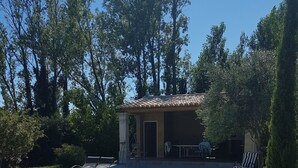 A backyard with a swimming pool, a patio area, and a small building with a tiled roof.