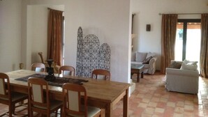 Un coin repas avec une table et des chaises en bois, un paravent décoratif en métal, et un espace salon avec un canapé et une fenêtre.