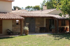 Un edificio de piedra con techo de tejas, un banco de madera y una mesa con sillas afuera.