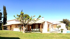 Une maison à deux étages avec une piscine, une terrasse dotée de chaises et un grand arbre dans le jardin.