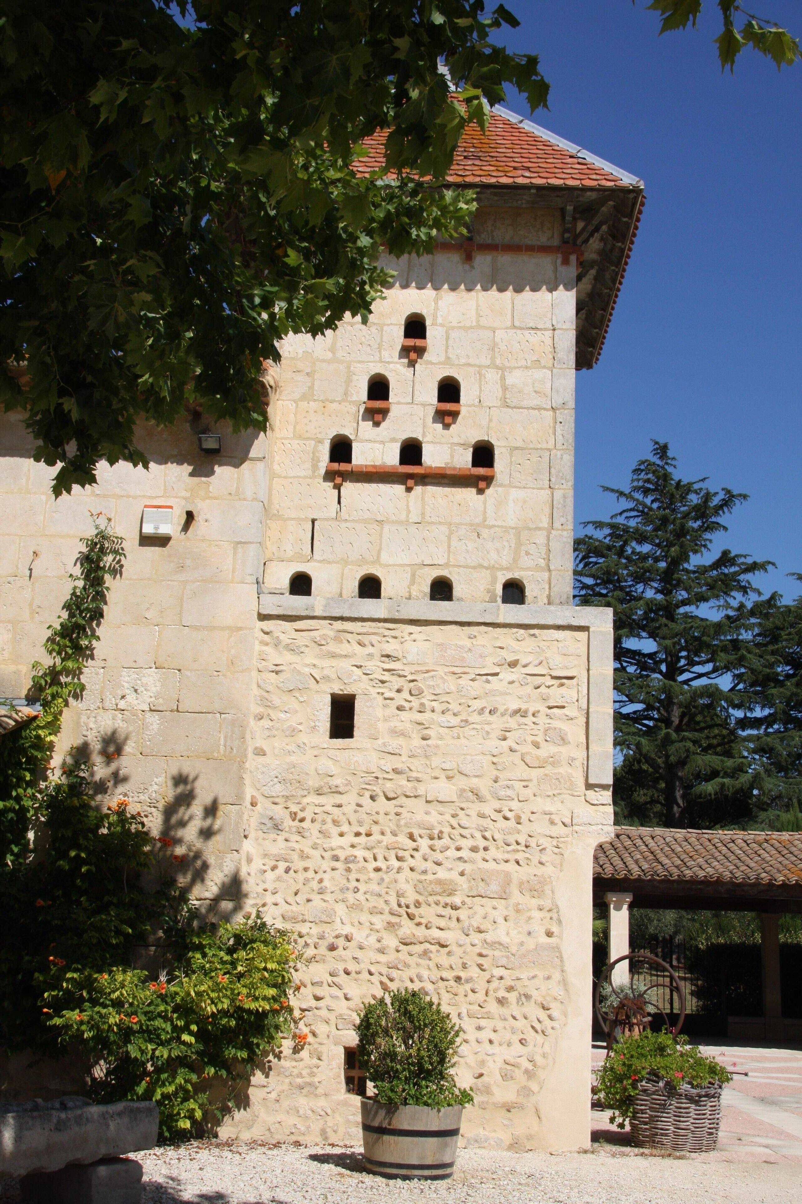 Ein Gebäude aus Stein mit einem Turm, einem überdachten Bereich und Topfpflanzen.