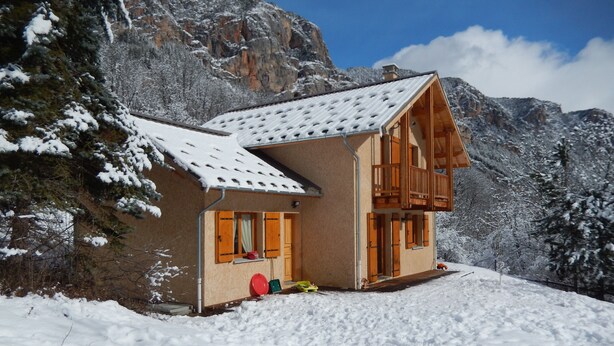 Ein Chalet mit einem geneigten Dach, einem Holzbalkon und Blick auf schneebedeckte Berge.