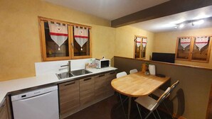 Eine kleine Küche mit Geschirrspüler, Mikrowelle und Spüle. Ein Holztisch mit vier Stühlen steht bereit. Die Küche verfügt über Holzschränke und ein Fenster mit Vorhang.