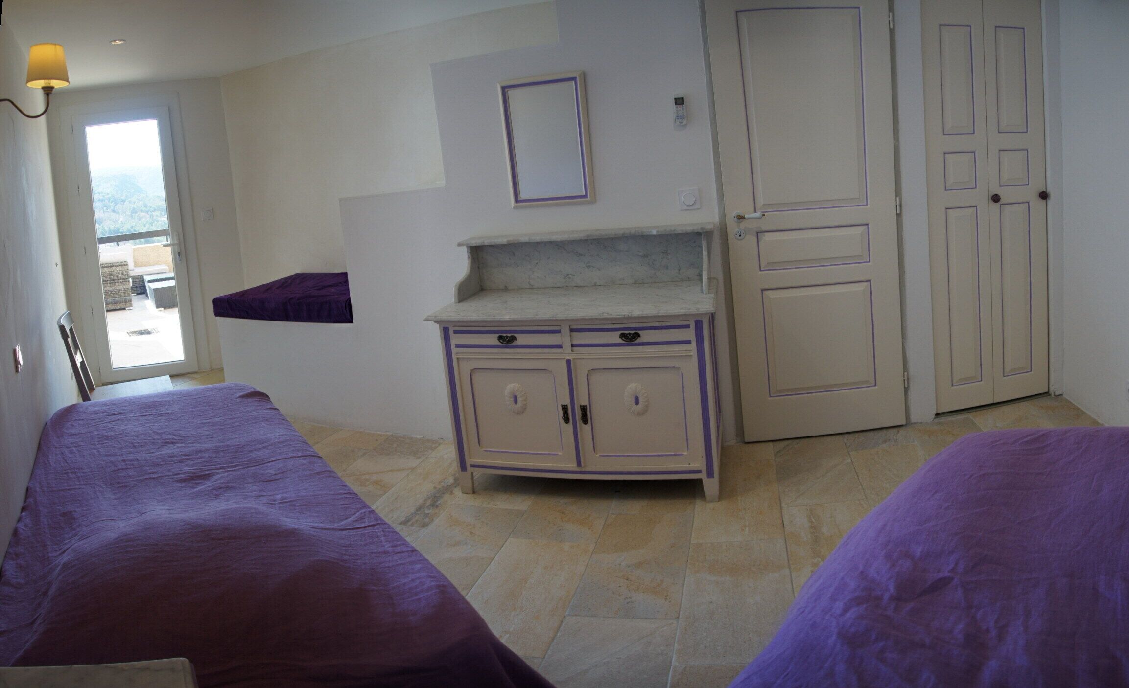 A room with two beds, a small cabinet, a door, and a window.