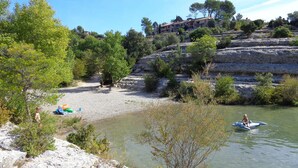 A rocky riverbank with a clear view of a building with multiple balconies in the background. - Apartment for 6 in Esparron-de-Verdon, with a wonderful lake view (Esparron-De-Verdon)