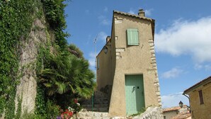 A stone building with a green door and a small window, surrounded by lush greenery and flowering plants. - Apartment for 6 in Esparron-de-Verdon, with a wonderful lake view (Esparron-De-Verdon)