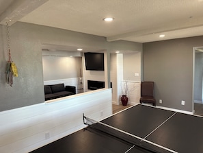 A room with a ping pong table, a sofa, a TV, and a fireplace.