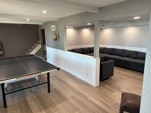Une pièce avec une table de ping-pong, un canapé d’angle et un escalier.