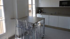A modern kitchen with white cabinets, a stainless steel sink, and a built-in microwave. There are two transparent chairs around a wooden table. - Place of the Strings in the heart of St Tropez apartment T2 new 2/4 with parking (Saint-Tropez)