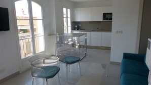 A modern kitchen with white cabinets, a dining area with clear chairs, and a large window. - Place of the Strings in the heart of St Tropez apartment T2 new 2/4 with parking (Saint-Tropez)