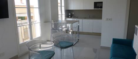 Cozinha moderna com armários brancos, espaço de jantar com cadeiras transparentes e uma janela grande.