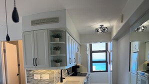 A modern kitchen with white cabinetry, a central island, a view to the sea, and a patterned floor.