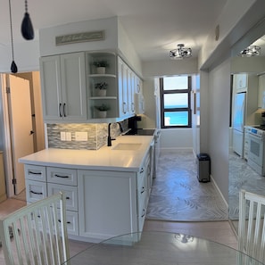 A modern kitchen with white cabinetry, a central island, a view to the sea, and a patterned floor.