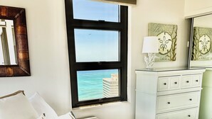 A bedroom with a bed, a dresser, a window with a view of the ocean, and a mirror.
