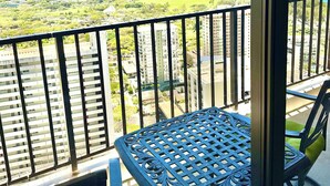 A balcony with a table and chairs, overlooking a coastal landscape with buildings and a mountain.