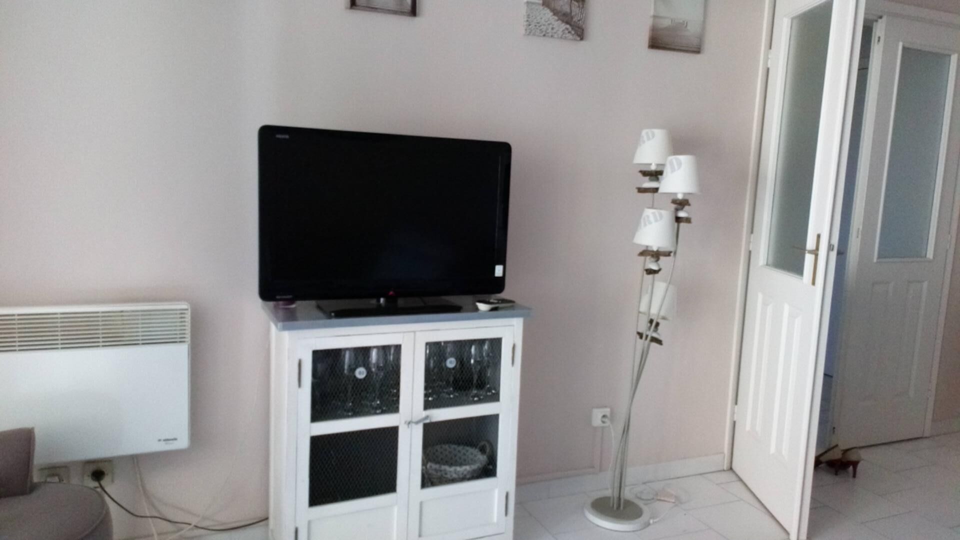 Een kamer met een televisie op een kast, een radiator, een vloerlamp en een deur.