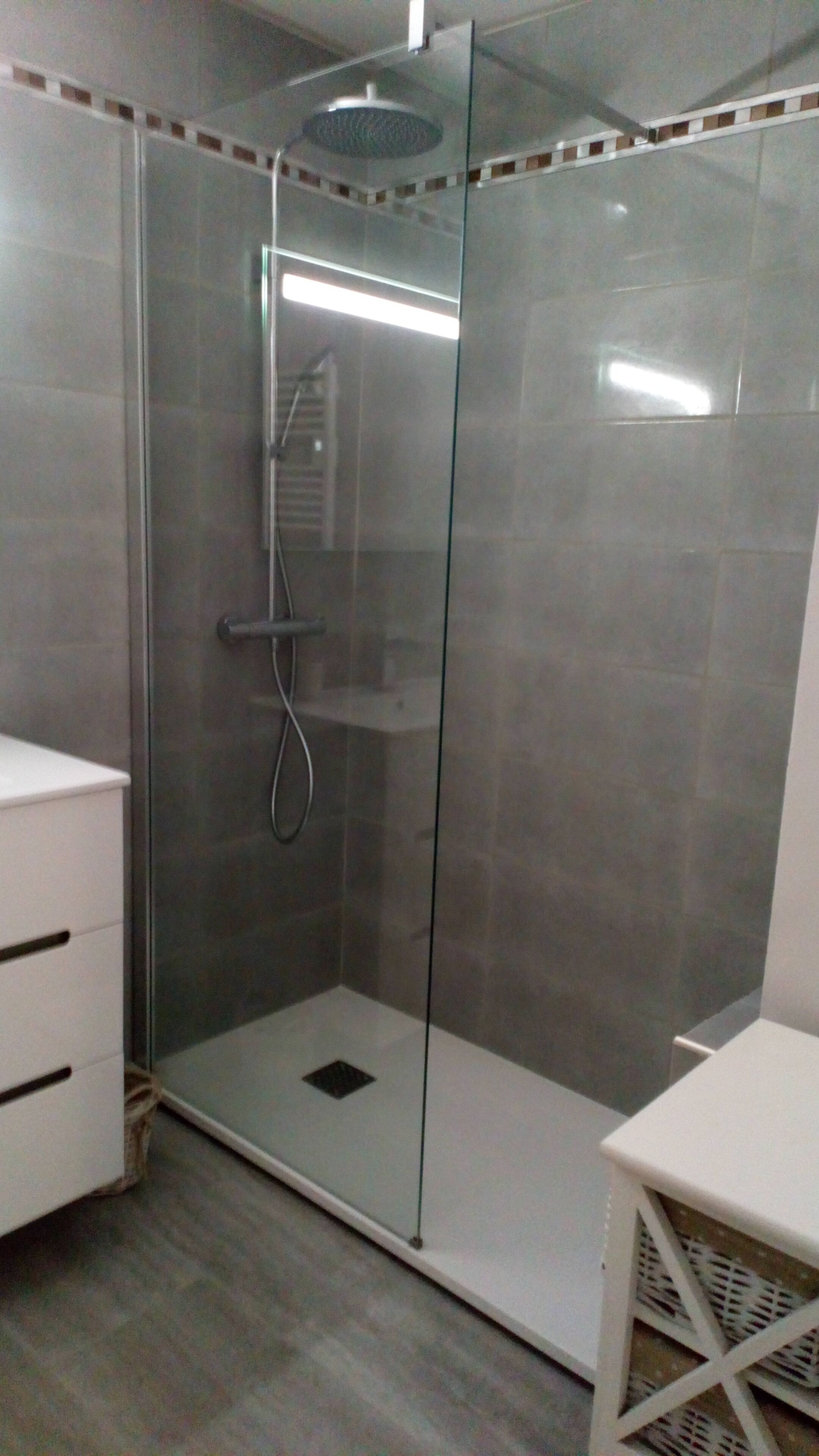 A glass-enclosed shower with a white sink and a white chair.