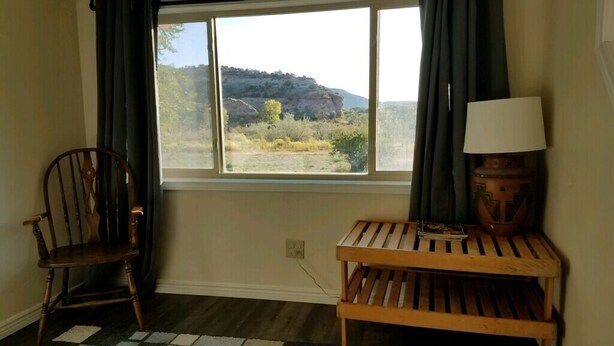 Ein Zimmer mit großem Fenster, einer hölzernen Bank, einem Stuhl und einer Lampe.
