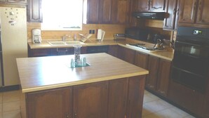 Eine Küche mit Holzschränken, einer Kochinsel, einem Kühlschrank, einem Herd und einer Spüle.
