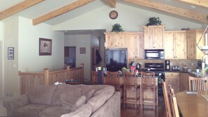 A spacious living room with a large sectional sofa, wooden ceiling beams, and a kitchen area with wooden cabinets and modern appliances. - Ski, Mountains, Lake: 5 BR Vacation House at Wolf Creek Ut, Many Amenities (eden)