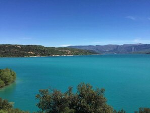 A coastal landscape with a clear view of a turquoise sea, green hills, and a tree line in the foreground. - Charming house near the Sainte Marie Moustiers Sainte Croix Lake (Moustiers-Sainte-Marie)