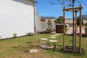 A backyard with a white wall, a wooden pergola, and a stone pathway leading to a door.