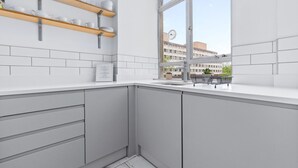 A modern kitchen with white cabinets, wooden shelves, and a large window offering a view of the city.