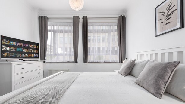 A modern bedroom with a large bed, a flat-screen TV, and a view of the city through large windows.