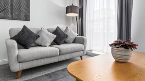 A modern living room with a grey sofa, patterned cushions, a wooden coffee table, and a potted plant.