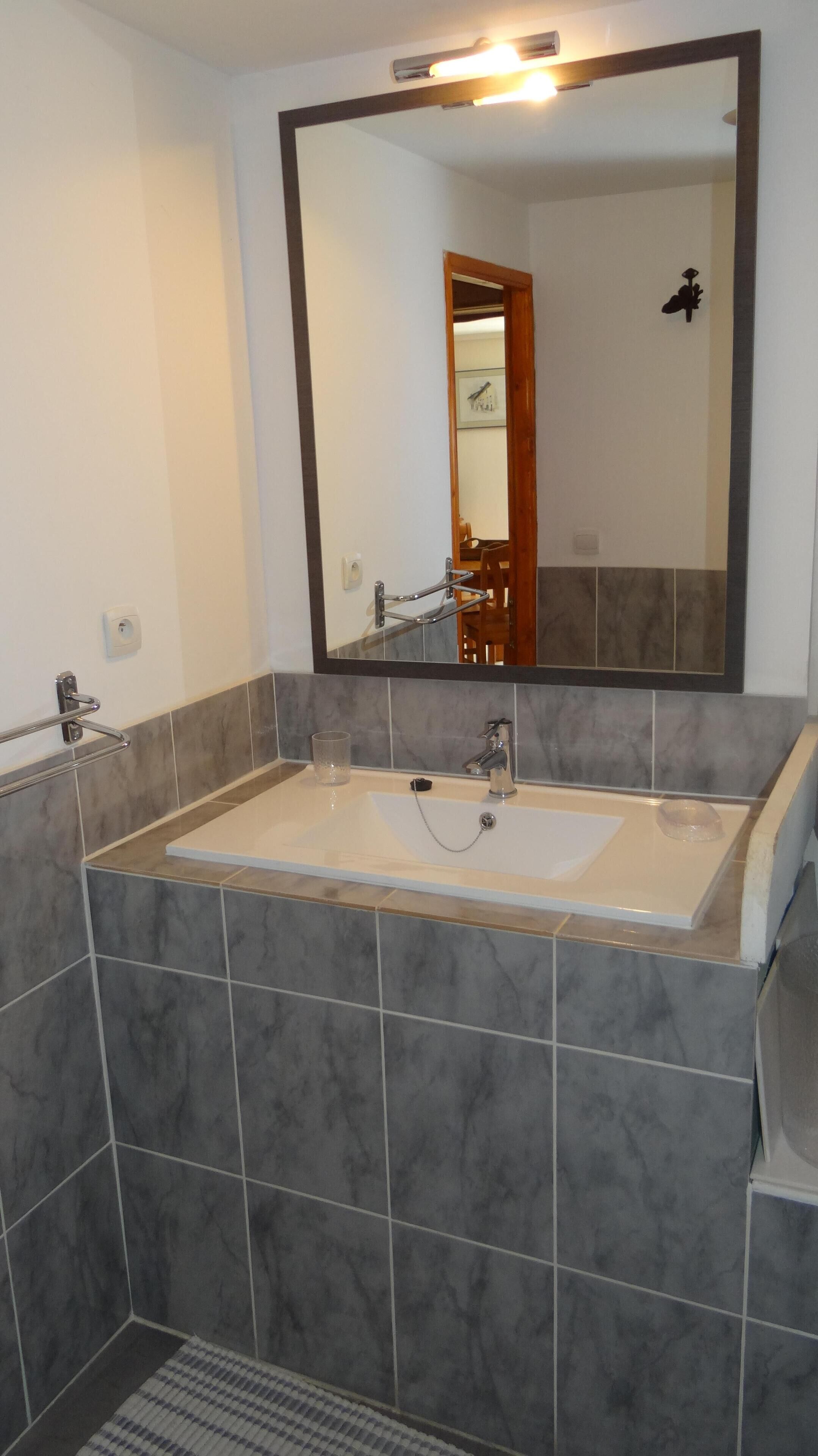 Une salle de bain dotée d’un grand miroir, de deux lavabos et d’un espace douche.