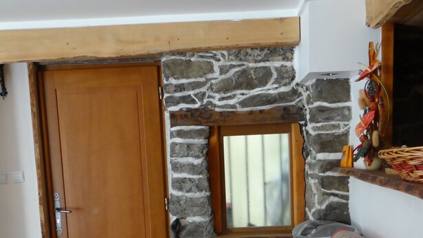 Una habitación con pared de piedra, puerta de madera, ventana y cama con colcha estampada.