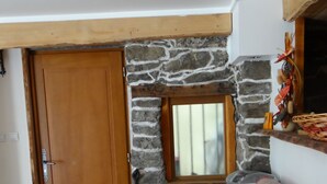 A room with a stone wall, a wooden door, a window, and a bed with a patterned blanket.