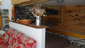 Una habitación acogedora con pared de piedra, un banco de madera, un florero de metal con flores secas y una cesta de mimbre.