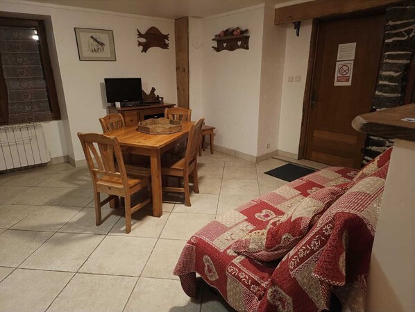 Ein Essbereich mit einem Holztisch und Stühlen, einem Fernseher auf einem Schrank und einem gemusterten Teppich.