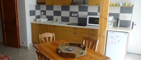 A compact kitchen with wooden cabinets, a microwave, and a refrigerator. There is a dining table with chairs and a wooden tray on it.