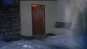 Exterior nevado de un edificio con puerta de madera y pared de piedra.